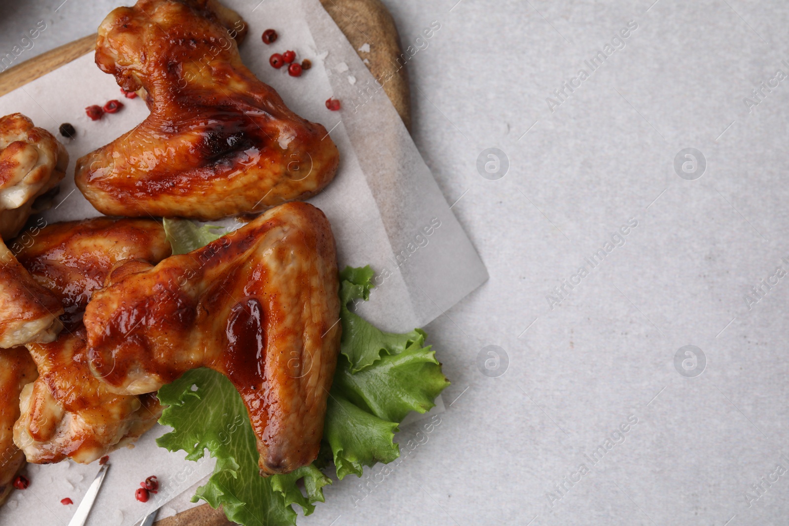 Photo of Fresh marinated chicken wings and lettuce on light table, top view. Space for text