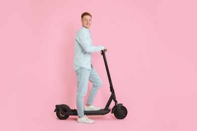 Photo of Happy man with modern electric kick scooter on pink background