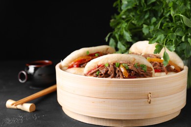 Photo of Delicious gua bao in bamboo steamer on black table