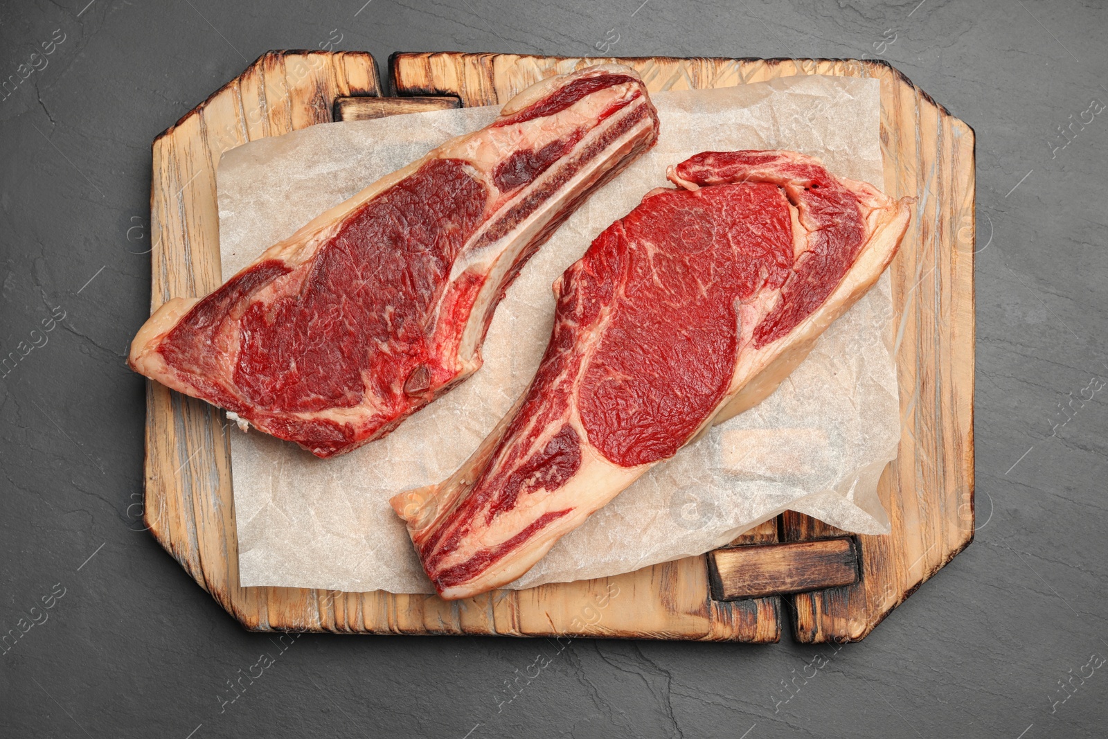 Photo of Wooden board with raw beef meat on black table, flat lay