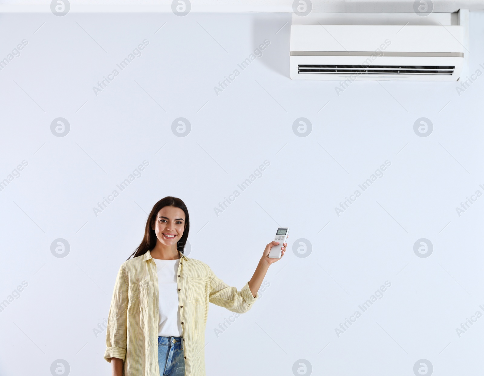 Photo of Young woman turning on air conditioner against white background