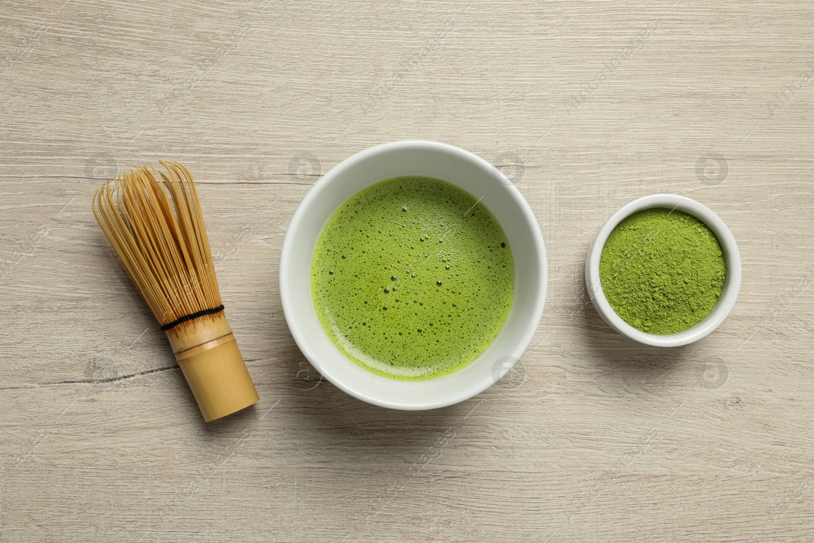 Photo of Cup of fresh matcha tea, bamboo whisk and green powder on wooden table, flat lay