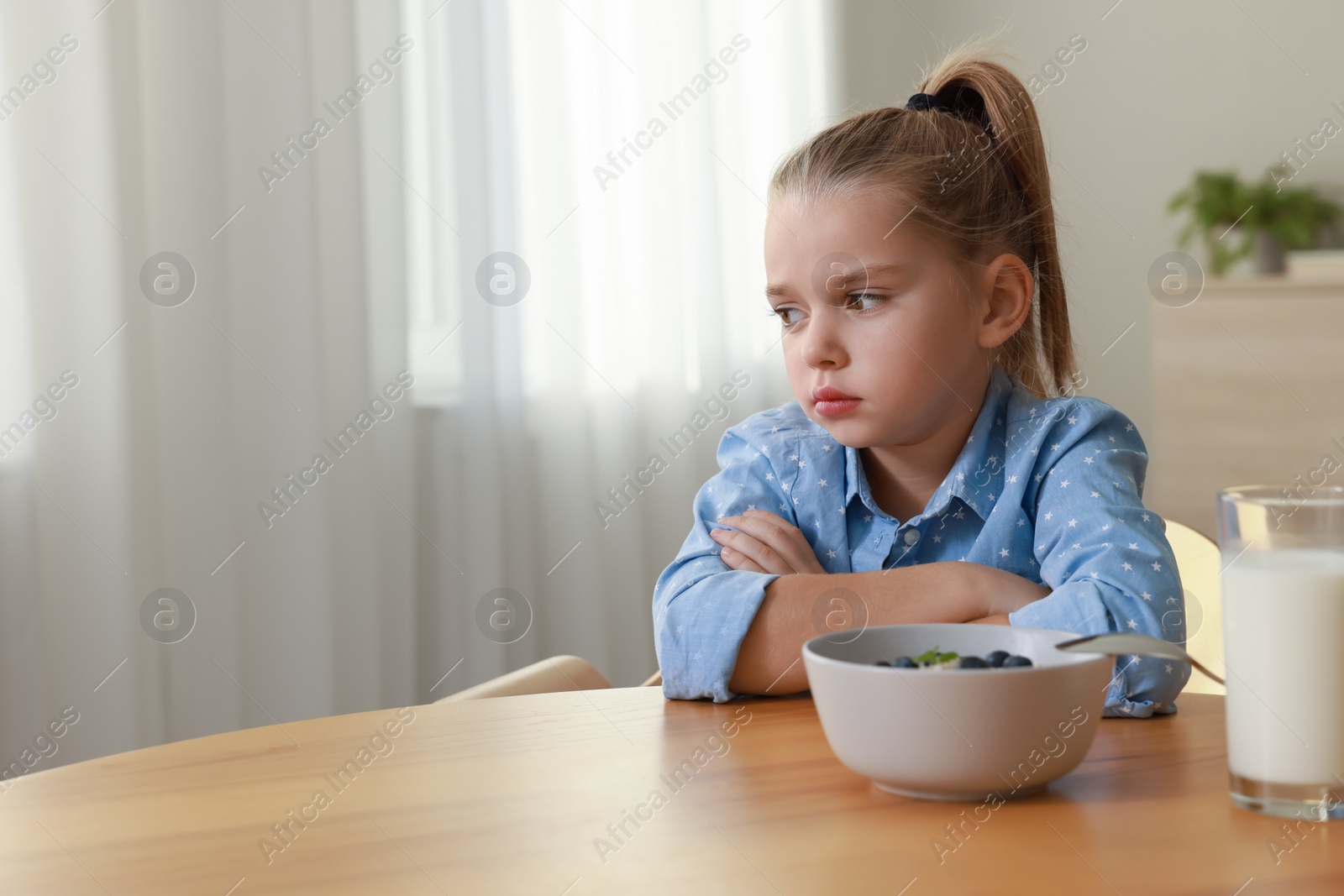 Photo of Cute little girl refusing to eat her breakfast at home, space for text