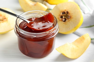 Eating tasty homemade quince jam from jar at white wooden table, closeup
