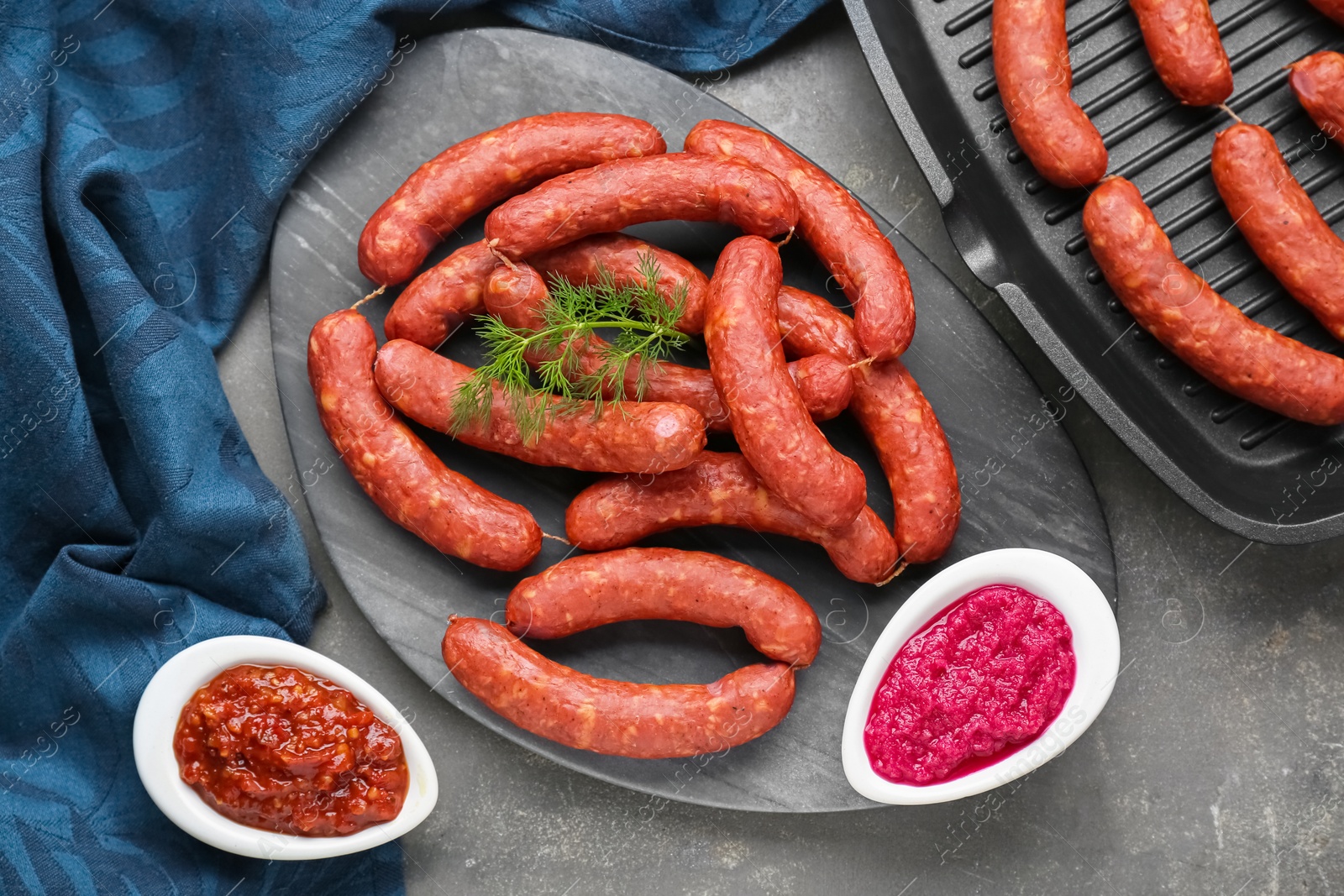 Photo of Delicious sausages, ketchup, dill and horseradish on grey table, flat lay