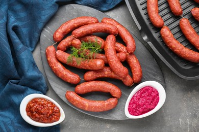 Photo of Delicious sausages, ketchup, dill and horseradish on grey table, flat lay