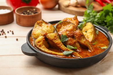 Photo of Tasty fish curry and ingredients on white wooden table, closeup. Indian cuisine