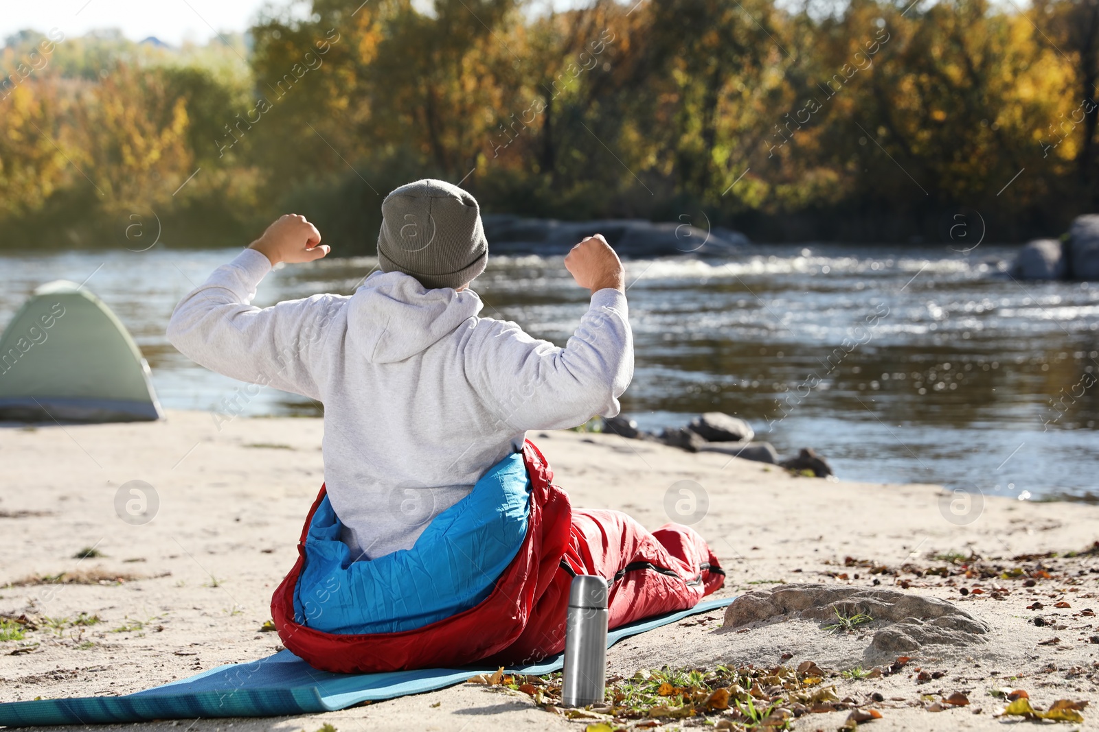 Photo of Male camper stretching in sleeping bag on wild beach. Space for text