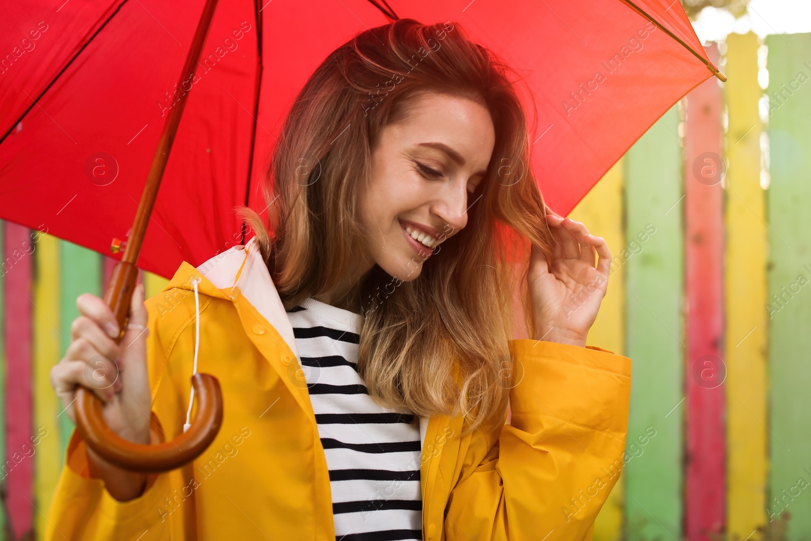 Photo of Beautiful young woman in stylish autumn clothes with red umbrella near color fence