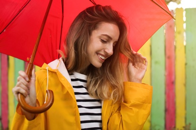 Photo of Beautiful young woman in stylish autumn clothes with red umbrella near color fence