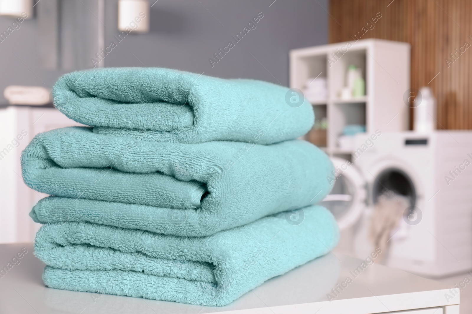 Photo of Stack of clean towels on table in laundry room. Space for text