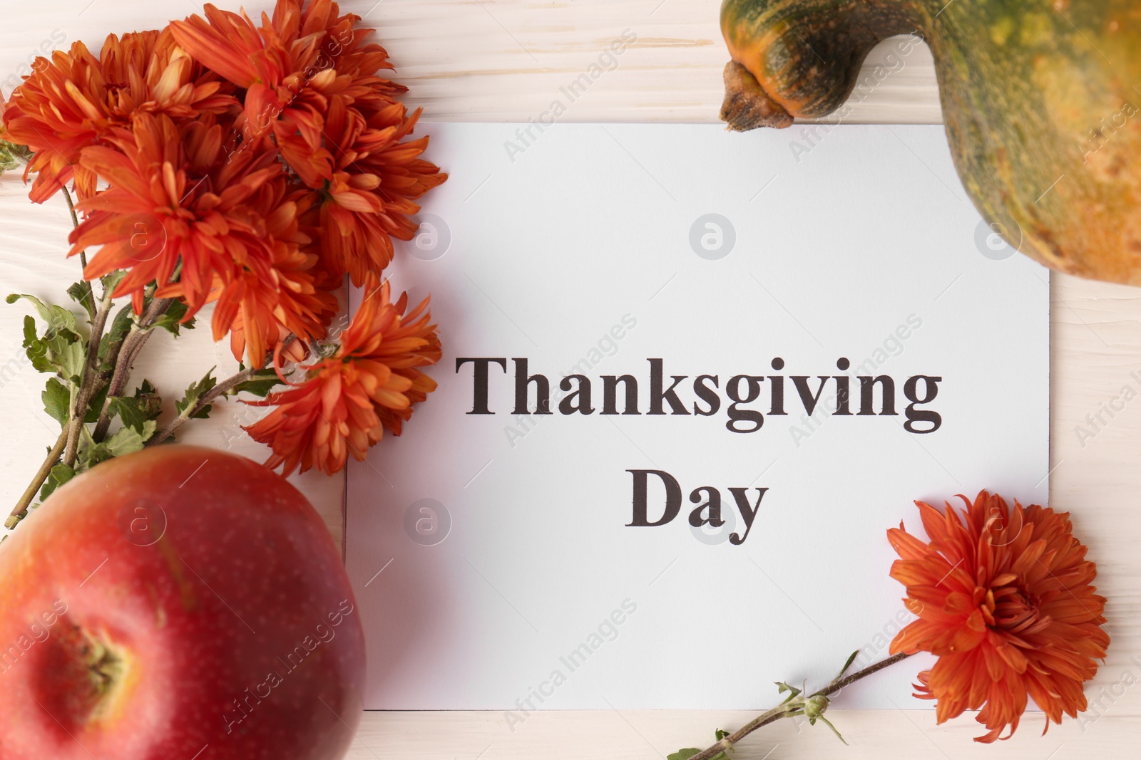 Photo of Thanksgiving day, holiday celebrated every fourth Thursday in November. Card, apple, pumpkin and chrysanthemum flowers on white wooden table, flat lay