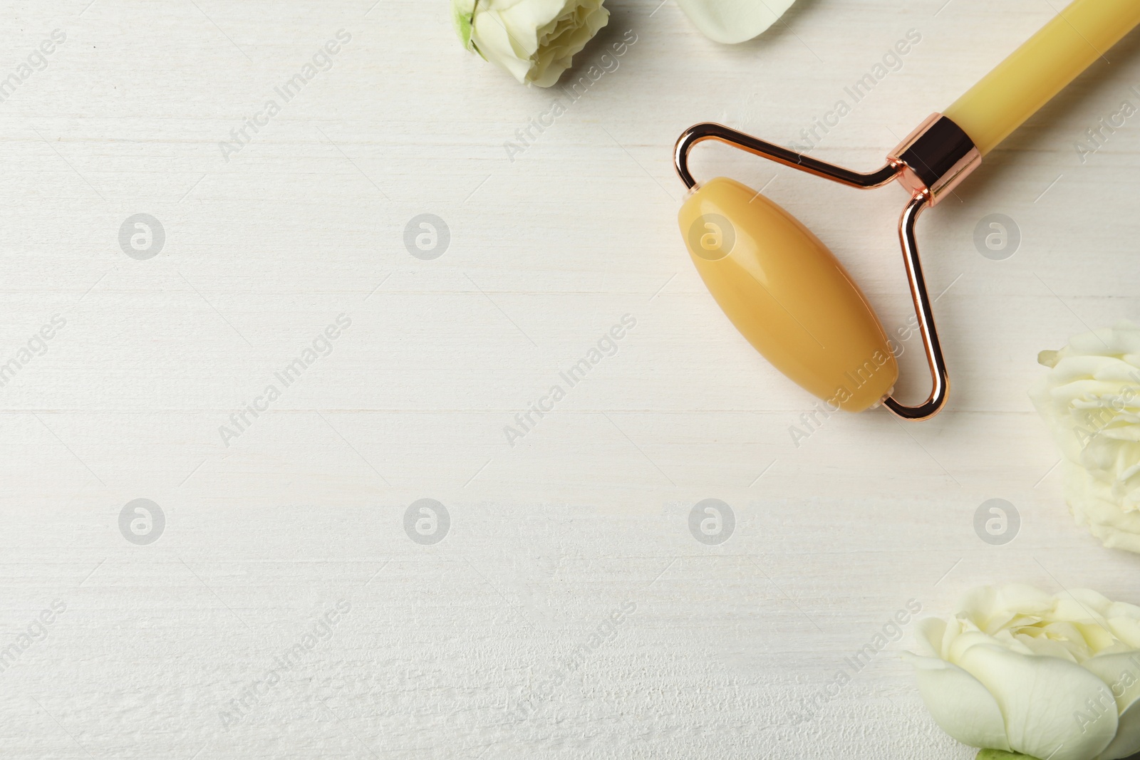 Photo of Natural jade face roller and flowers on white wooden background, flat lay. Space for text