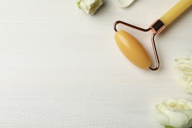 Natural jade face roller and flowers on white wooden background, flat lay. Space for text