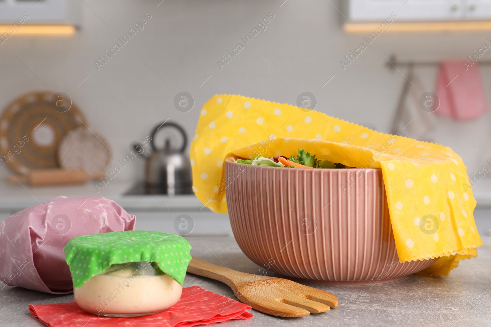 Photo of Bowl of fresh salad covered with beeswax food wrap on light grey table in kitchen