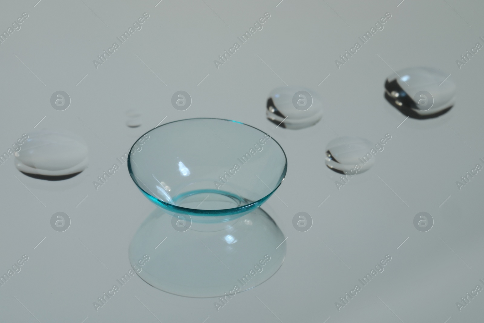 Photo of Contact lens and drops of water on white reflective surface