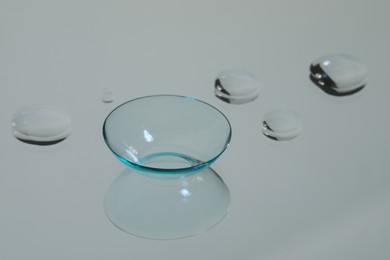 Photo of Contact lens and drops of water on white reflective surface