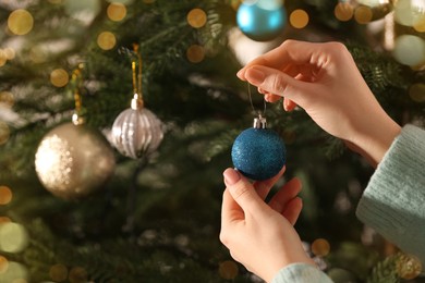 Woman decorating Christmas tree with beautiful light blue bauble, closeup