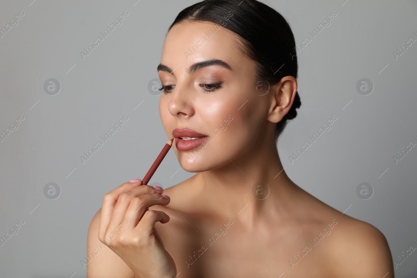 Photo of Pretty young woman applying beautiful nude lip pencil on grey background