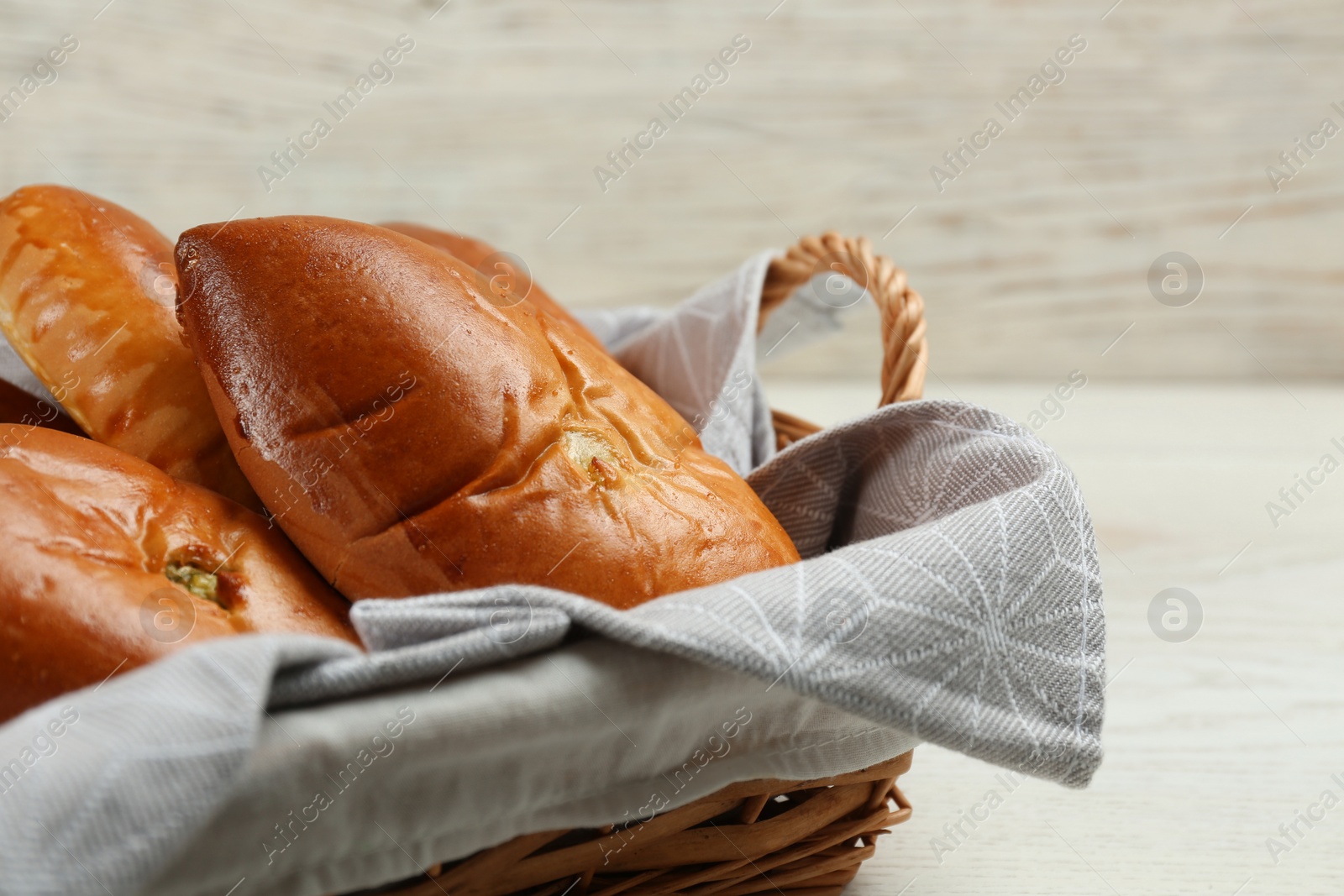 Photo of Wicker basket with delicious baked patties on white wooden table, closeup. Space for text