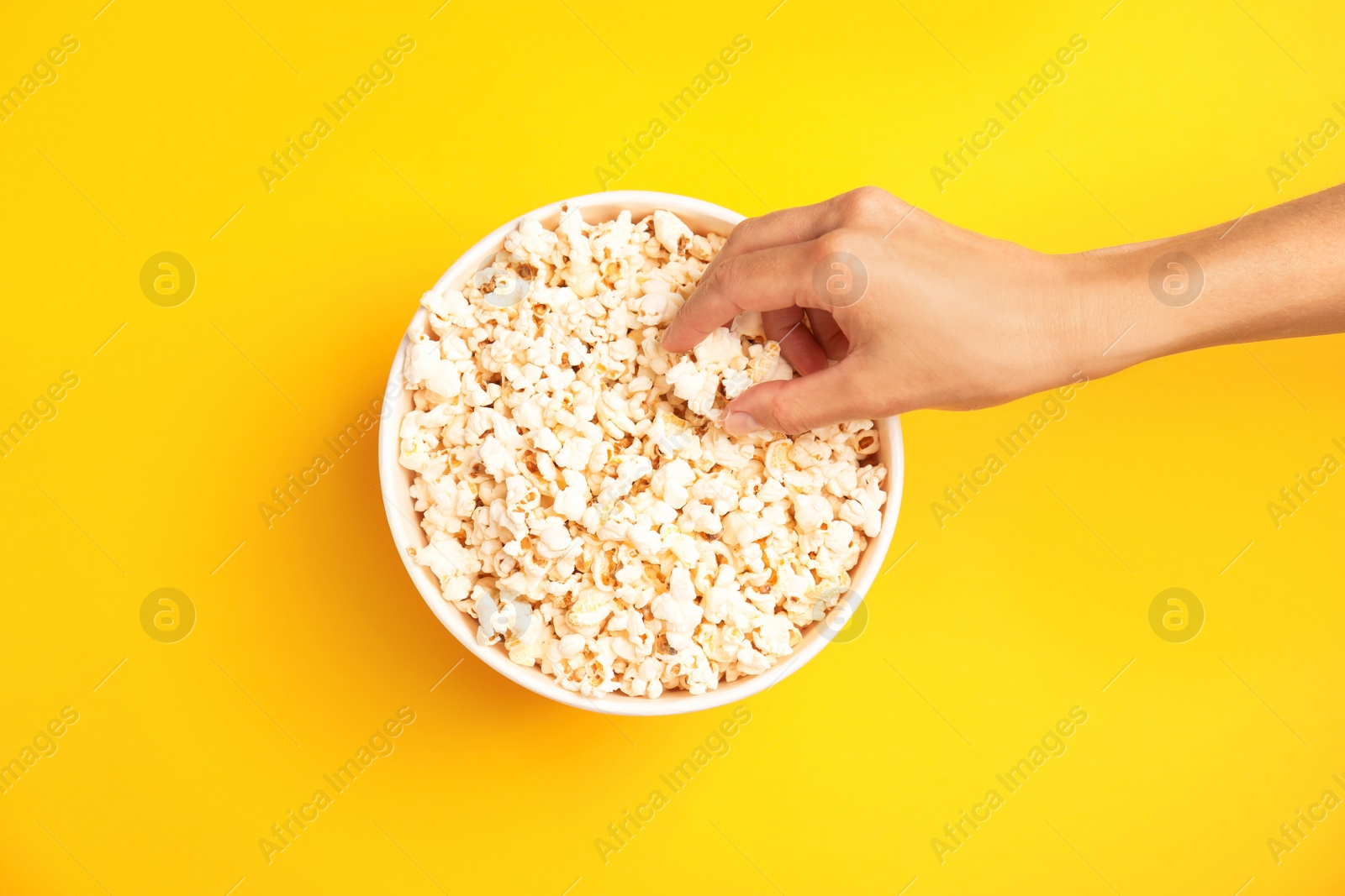 Photo of Woman with paper bucket of popcorn on color background, top view