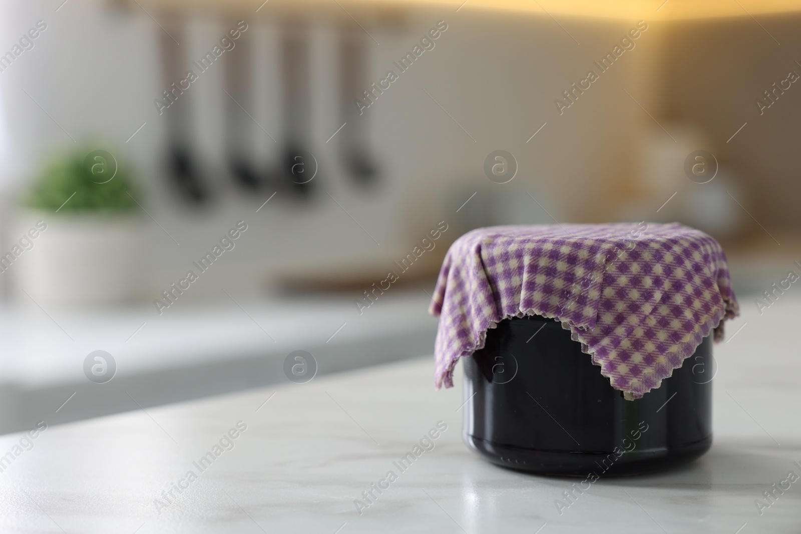 Photo of Jar of jam covered with beeswax food wrap on white table indoors, space for text