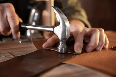 Photo of Man working with piece of leather at table, closeup