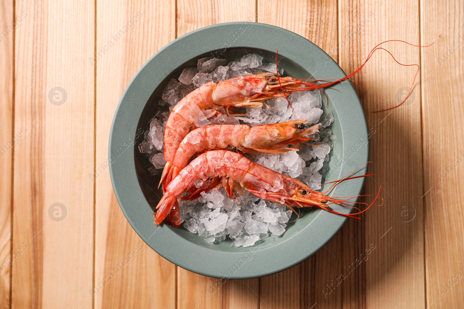 Photo of Fresh royal shrimps with ice on wooden table, top view