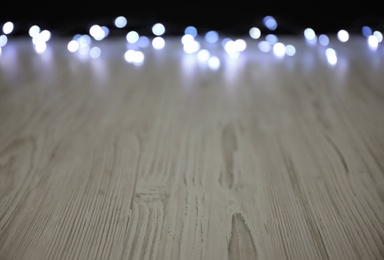 Blurred view of beautiful glowing lights, focus on wooden table. Space for text