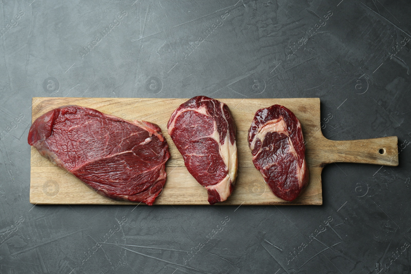 Photo of Wooden board with pieces of raw beef meat on grey table, top view