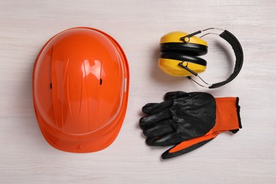 Hard hat, earmuffs and gloves on white wooden table, flat lay. Safety equipment