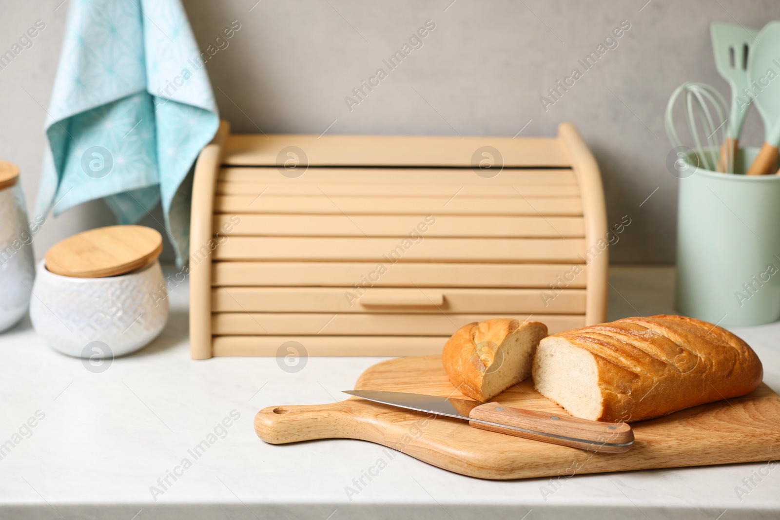 Photo of Wooden bread basket, freshly baked loaf on white marble table in kitchen