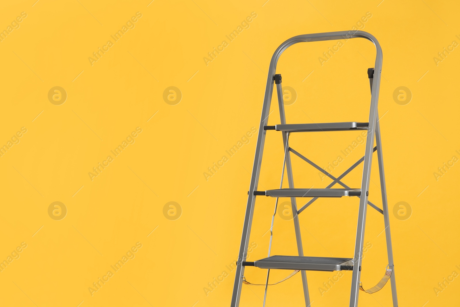 Photo of Modern metal stepladder on yellow background. Space for text