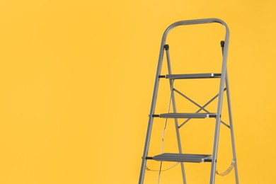 Modern metal stepladder on yellow background. Space for text