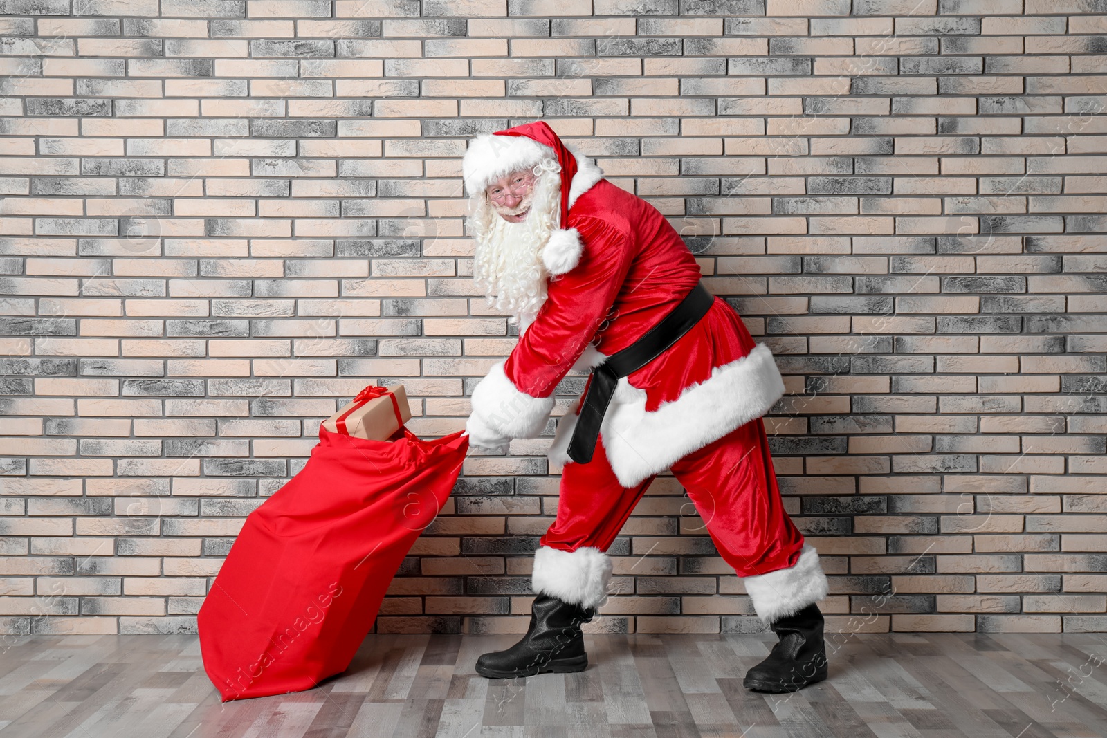 Photo of Authentic Santa Claus with big red bag full of gifts near brick wall