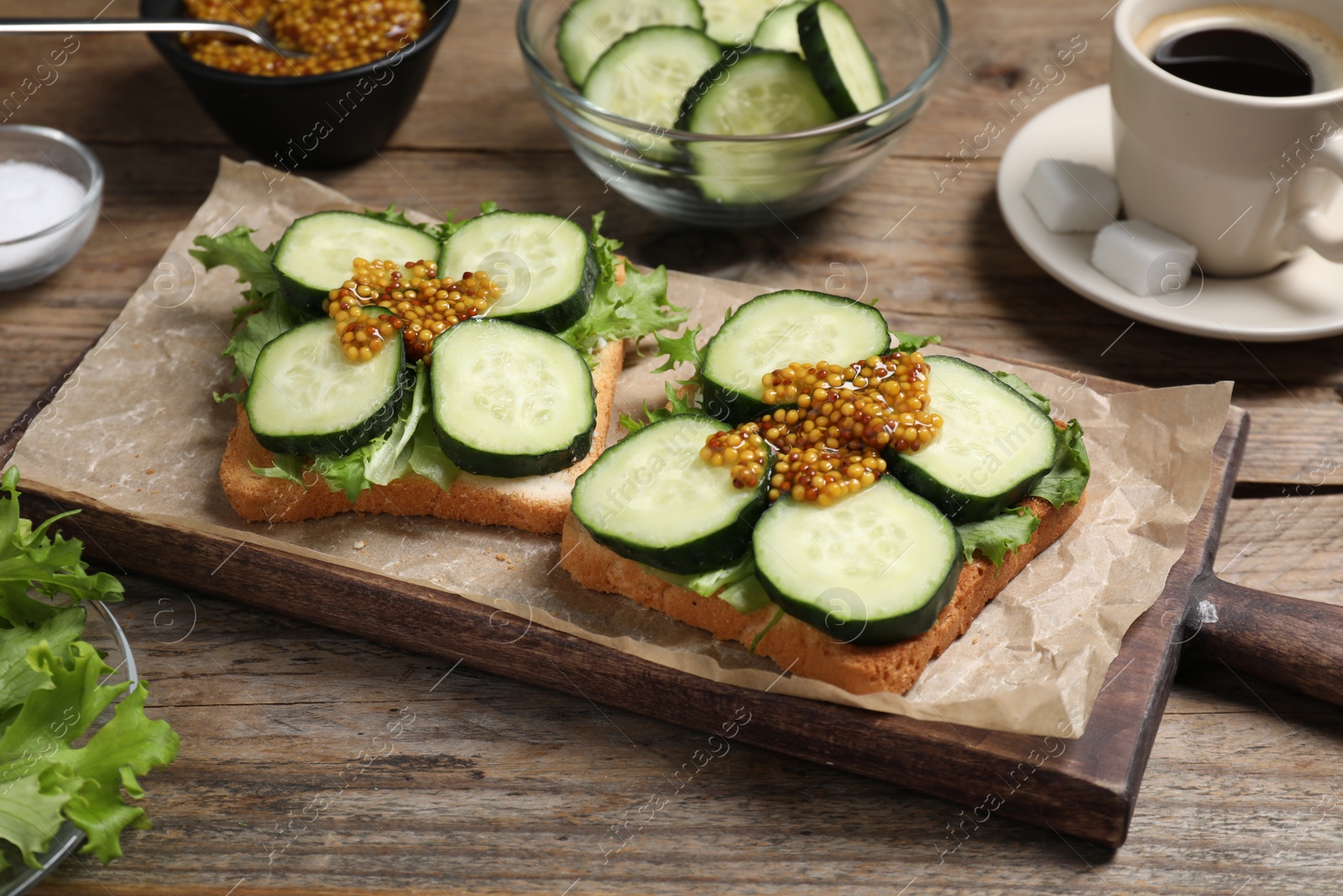 Photo of Tasty cucumber sandwiches with arugula, mustard and coffee on wooden table