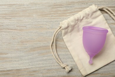 Photo of Menstrual cup with bag on light wooden background, top view. Space for text
