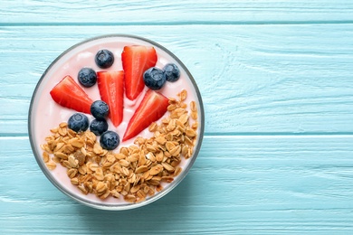 Photo of Bowl with yogurt, berries and granola on wooden background, top view