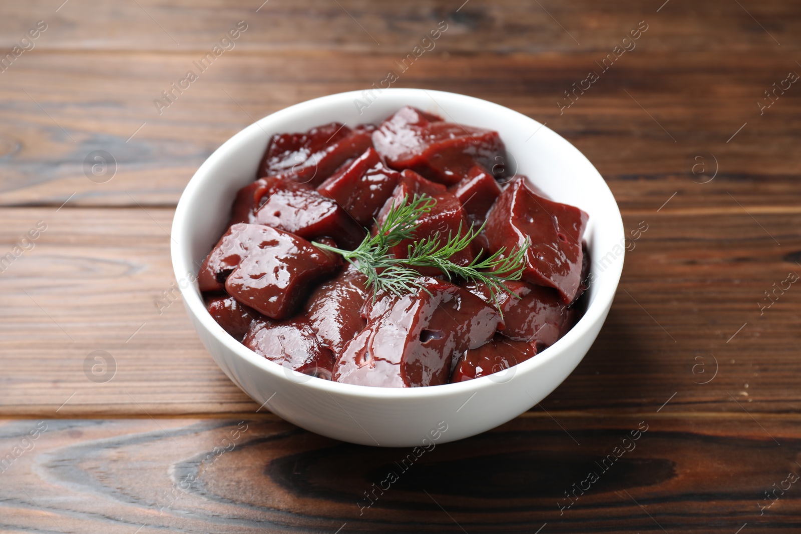 Photo of Cut raw beef liver with dill on wooden table, closeup