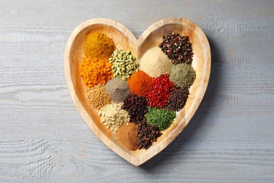 Photo of Heart shaped plate with different spices on grey wooden table, top view