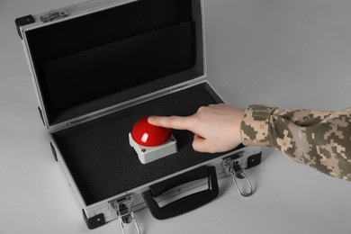 Photo of Serviceman pressing red button of nuclear weapon on light gray background, closeup. War concept