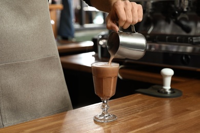 Photo of Barista pouring coffee into glass at bar counter, closeup