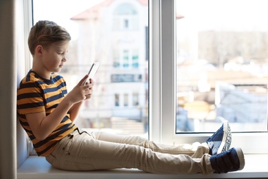Photo of Little child with smartphone on windowsill, space for text. Danger of internet