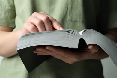 Woman reading holy Bible against light grey background, closeup