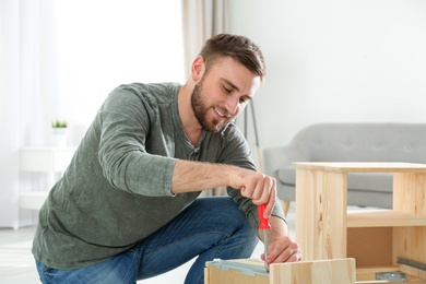 Photo of Young working man repairing drawer at home