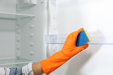 Worker in rubber gloves cleaning empty refrigerator, closeup