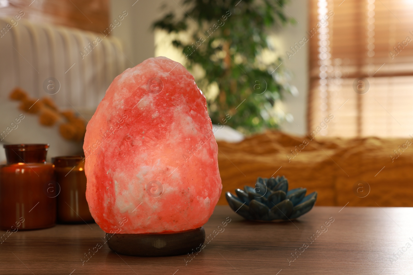 Photo of Beautiful Himalayan salt lamp, lotus figure and candles on wooden table in bedroom, space for text