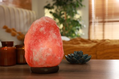 Photo of Beautiful Himalayan salt lamp, lotus figure and candles on wooden table in bedroom, space for text