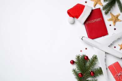 Photo of Flat lay composition with Christmas decorations, toy airplane and passport on white background, space for text. Winter vacation