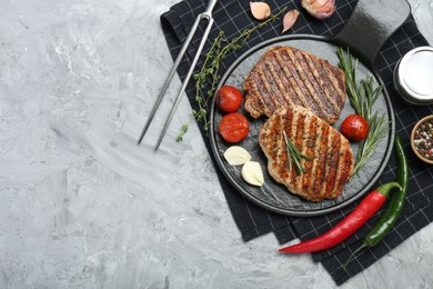 Delicious grilled pork steaks with spices and meat fork on gray textured table, top view. Space for text